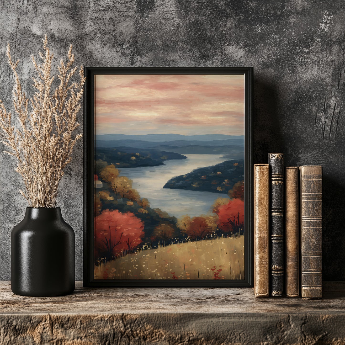 a framed painting of a serene landscape with a river, mountains, and trees, placed on a wooden shelf next to a vase with dried flowers.
