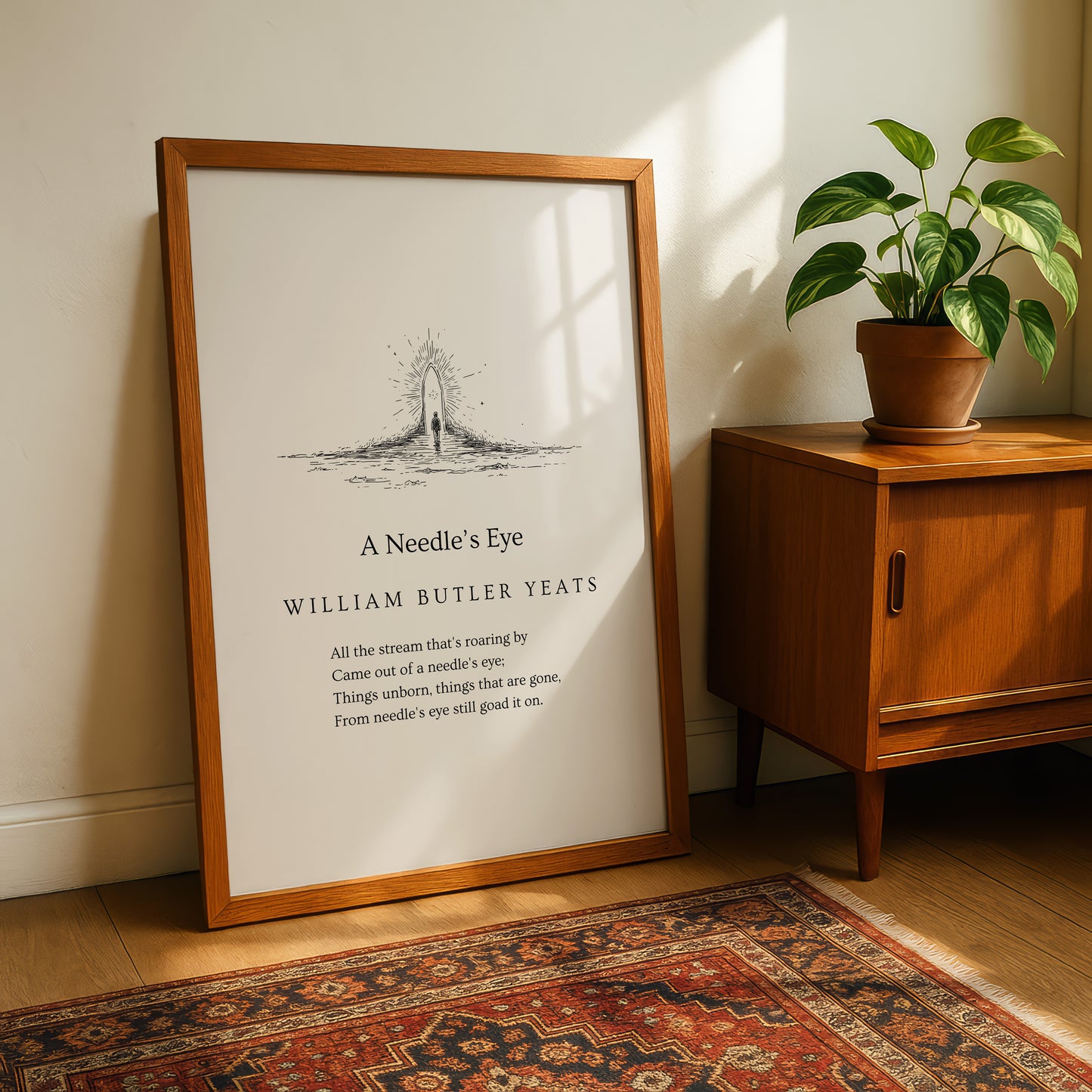 A framed print titled "A Needle's Eye" by William Butler Yeats, featuring a black and white illustration of a needle and thread, is displayed on a wooden cabinet next to a potted plant.