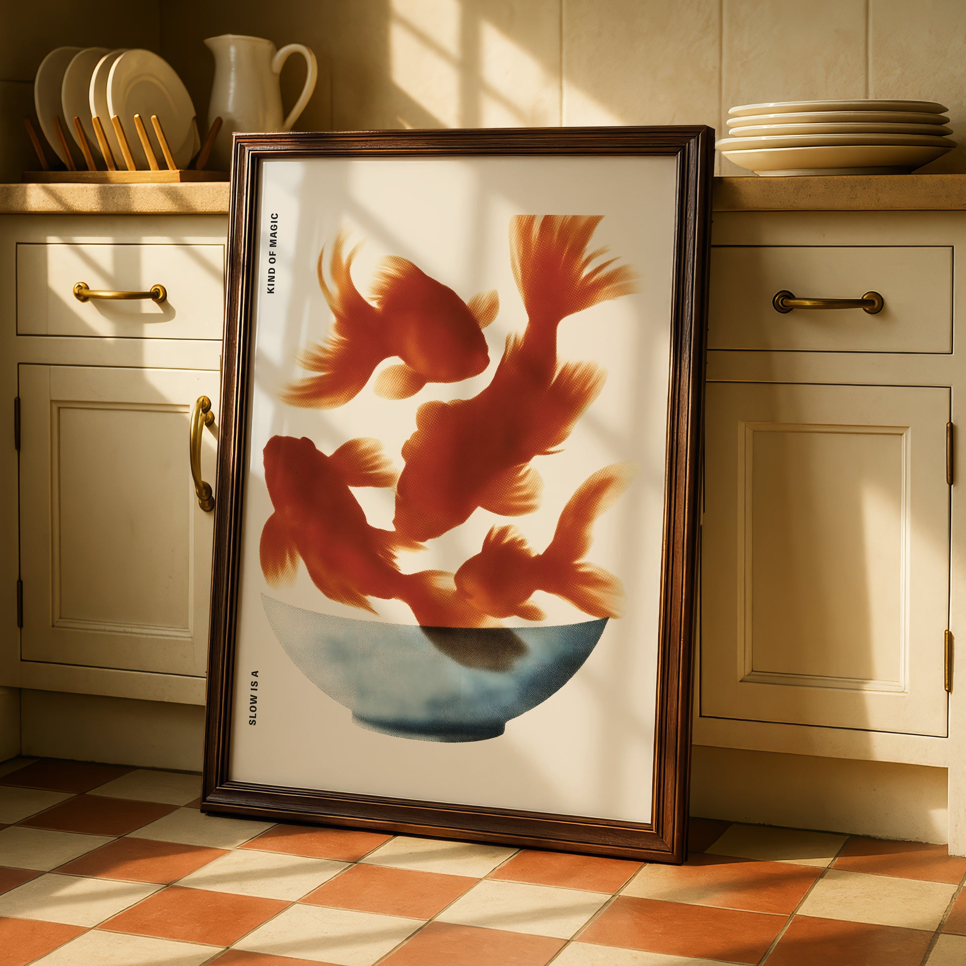 A framed print of a vibrant illustration of three goldfish swimming in a bowl is displayed on a kitchen counter.