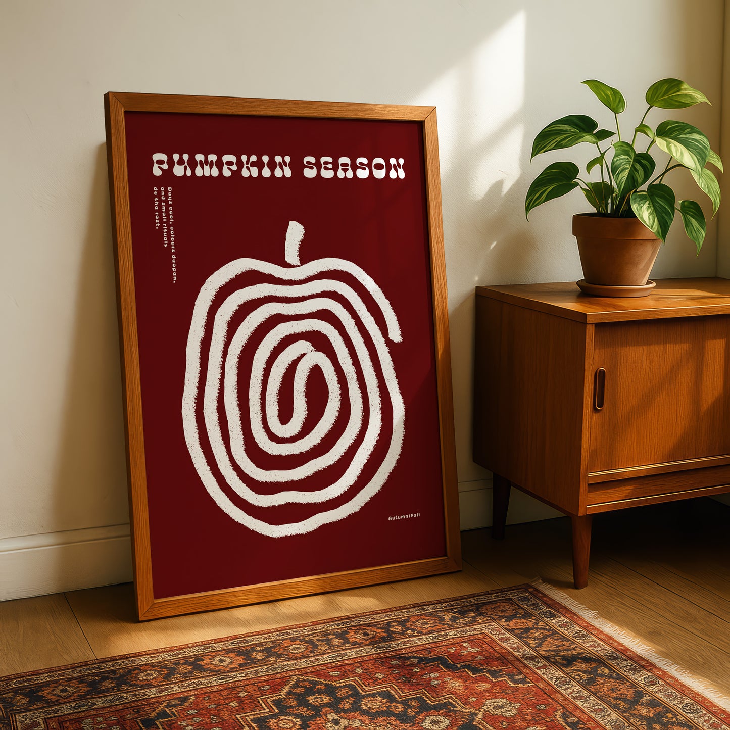 a framed poster of a spiral design on a red background, placed on a wooden floor next to a potted plant and a wooden cabinet.