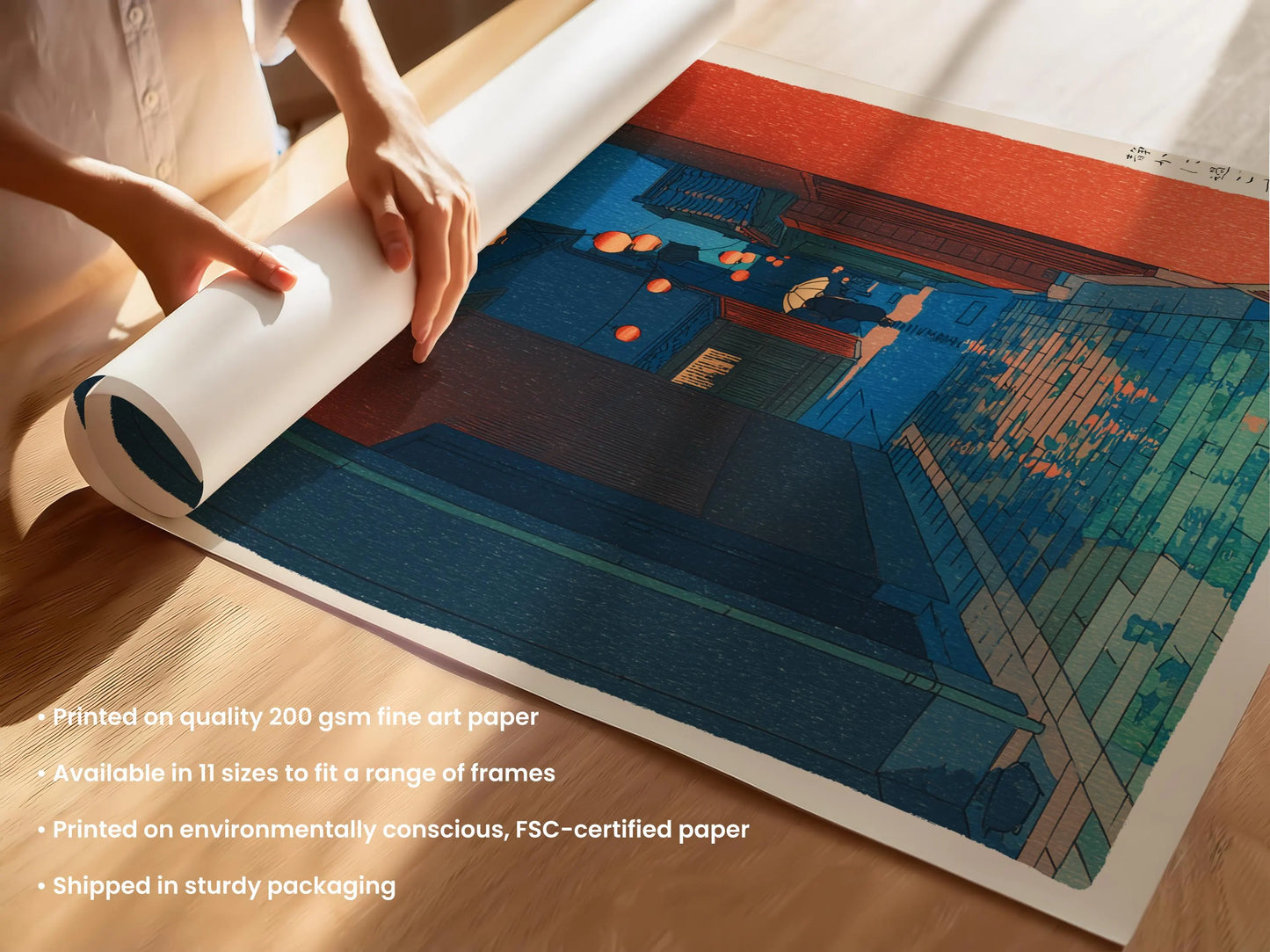 A person is rolling up a roll of 200-gram fine art paper, which is available in 11 sizes to fit a range of frames. The paper is printed on environmentally conscious, FSC-certified paper, and it is being shipped in sturdy packaging.