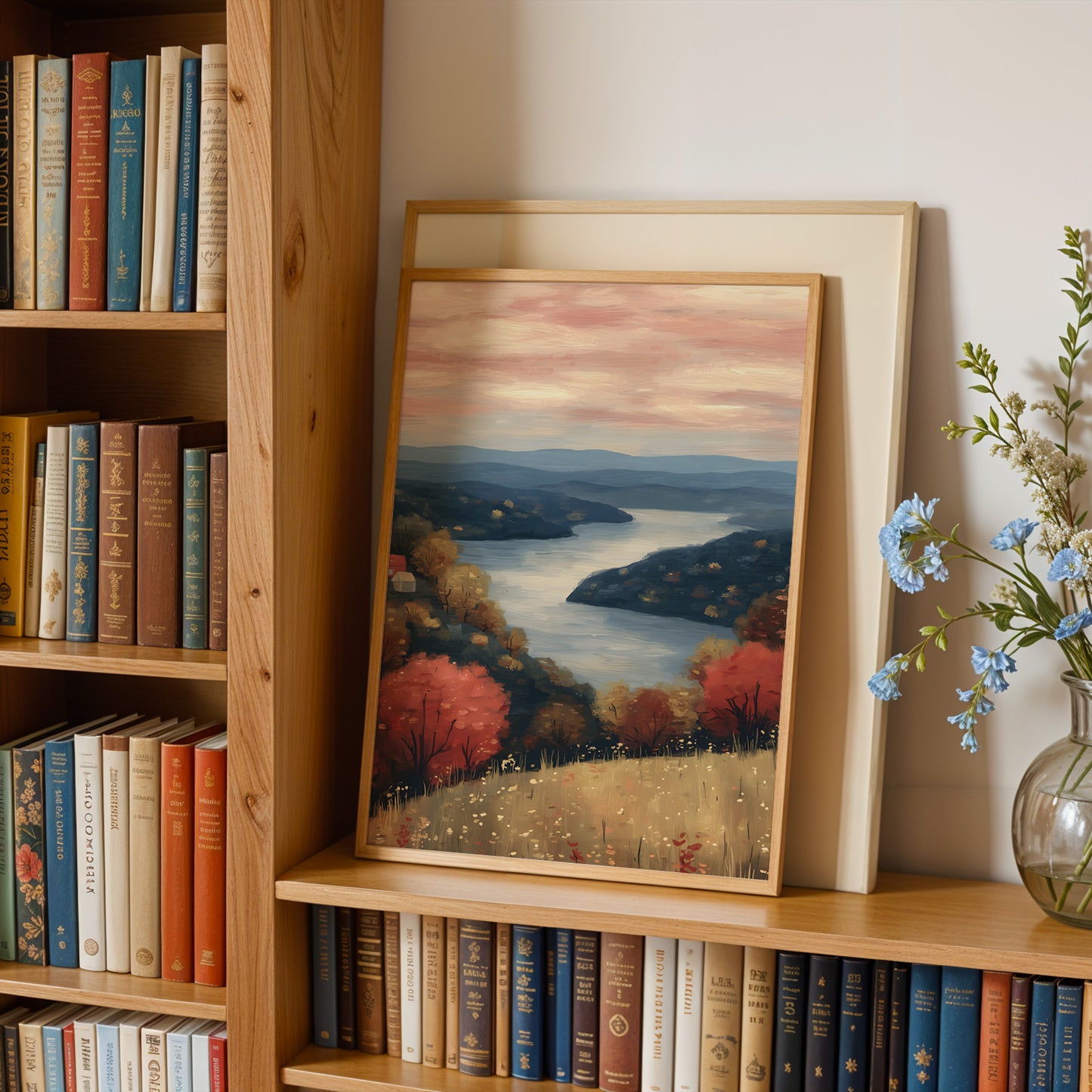 a wooden bookshelf filled with books, a framed landscape painting depicting a serene countryside scene, and a vase of blue flowers.