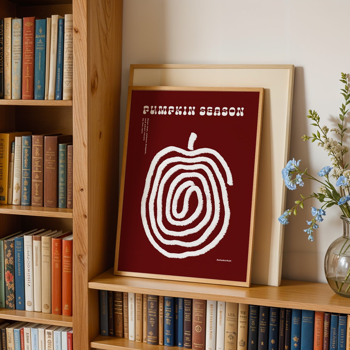a bookshelf with a framed poster of a spiral design on the shelf, surrounded by various books. There is also a vase of flowers on the right side of the bookshelf.