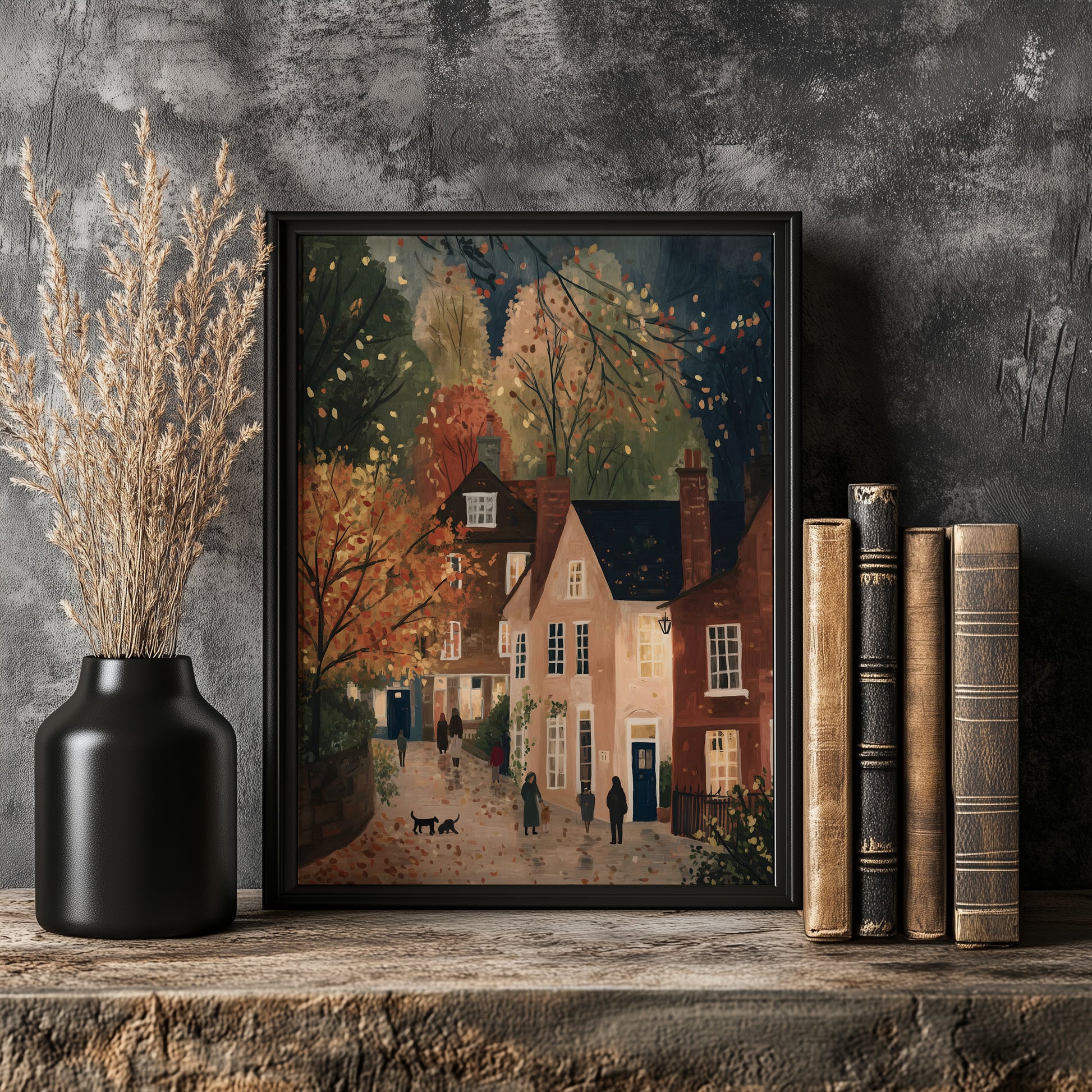 a framed painting of a quaint village scene, with a cobblestone street, colorful houses, and people walking along the street. The painting is displayed on a wooden shelf, accompanied by a black vase with dried flowers and a stack of books.