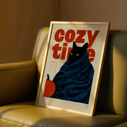 A framed poster of a cat wrapped in a blue blanket, with the text "cozy time" prominently displayed.
