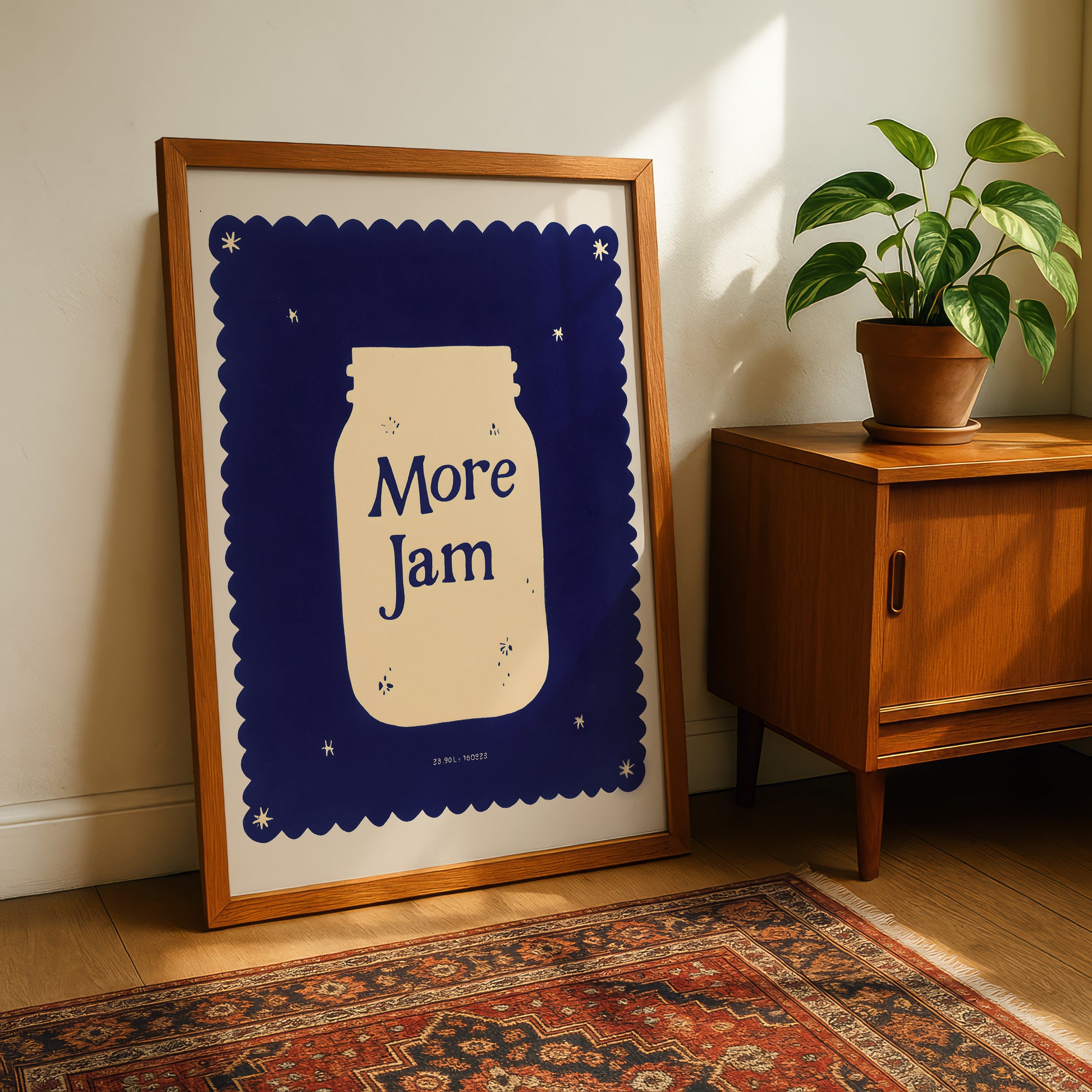 a framed poster with a jar design and the text "More Jam" on a wooden cabinet next to a potted plant.