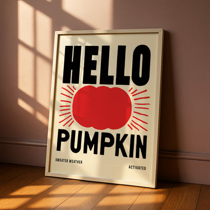 A framed poster with the text "HELLO PUMPKIN" and a red pumpkin graphic, placed on a wooden floor against a beige wall.
