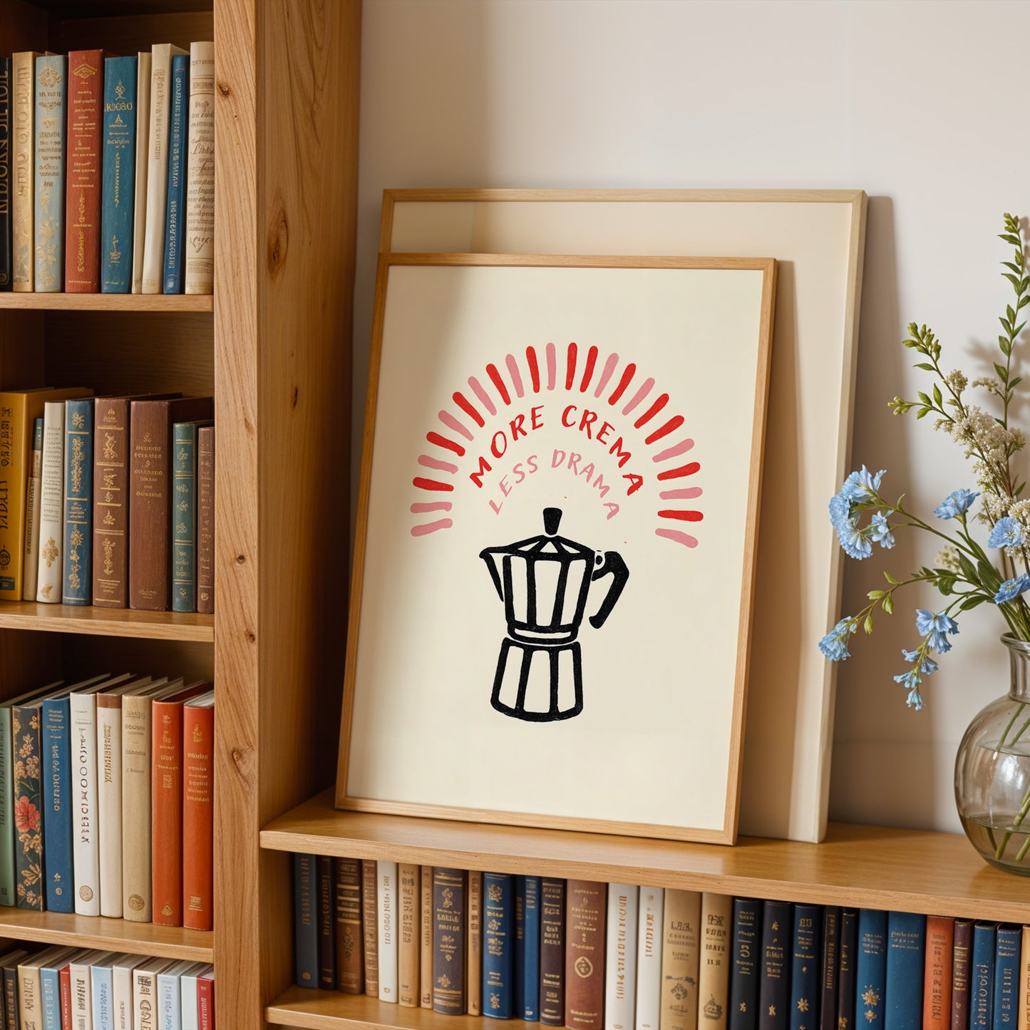 a bookshelf with a framed poster on it that says "MORE CREMA LESS DRAMA" in bold red and black text. The poster also includes a black silhouette of a coffee pot.