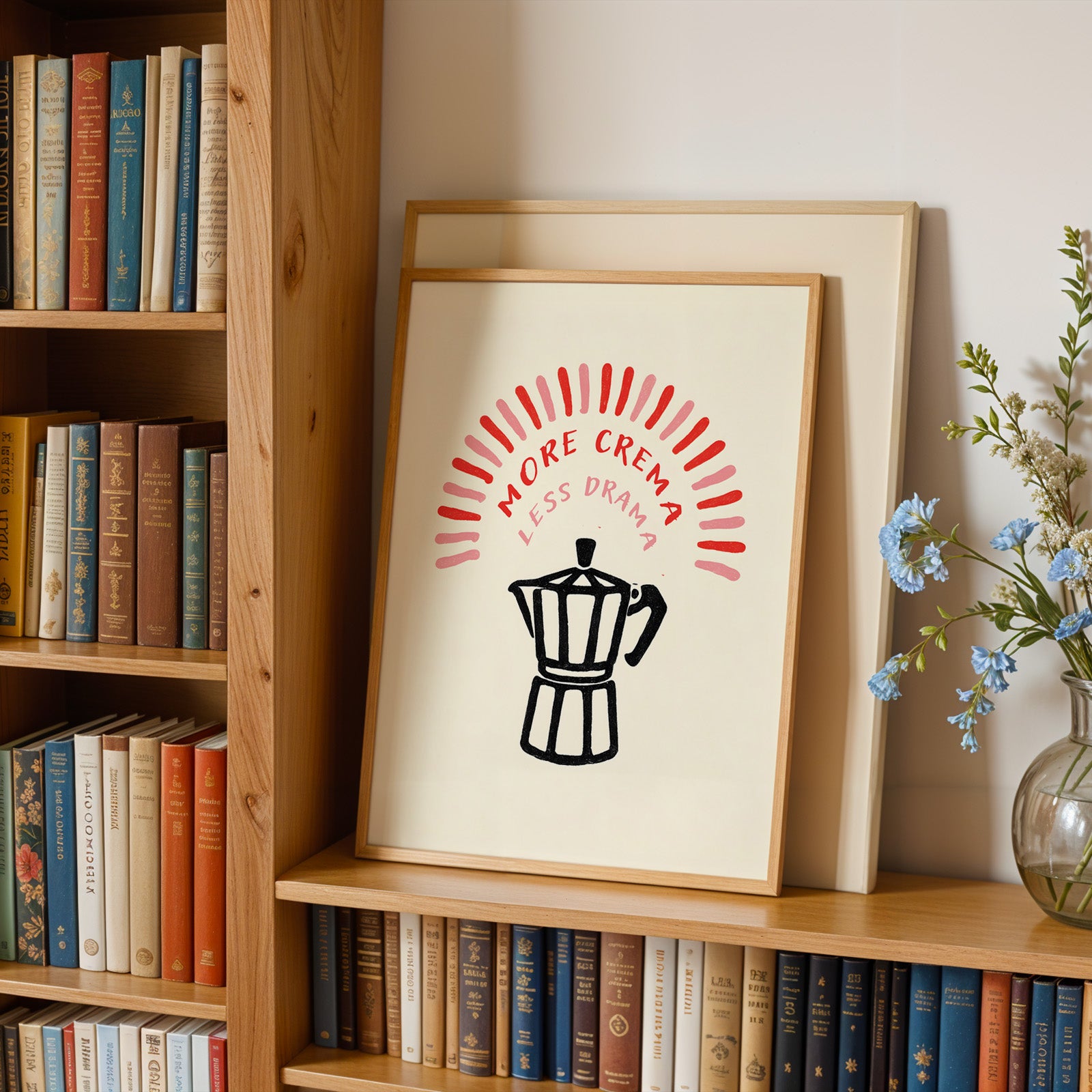 a bookshelf with a framed poster on it that says "MORE CREMA LESS DRAMA" in bold red and black text. The poster also includes a black silhouette of a coffee pot.