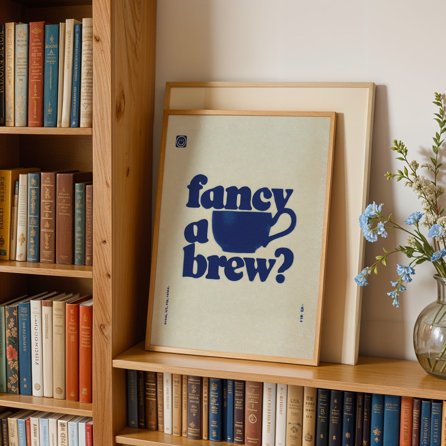 a bookshelf with a framed poster that reads "fancy a brew?" in blue text, surrounded by various books and a vase of flowers.