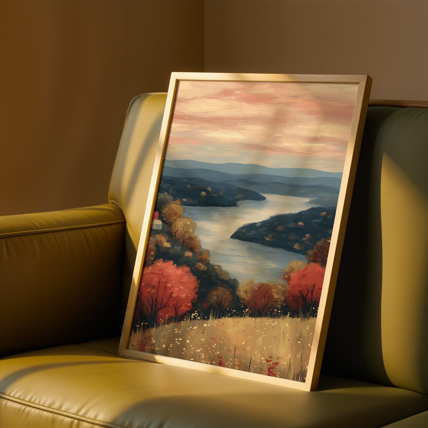 A framed painting depicting a serene landscape with a river, mountains, and trees in autumn colors is displayed on a beige leather couch.