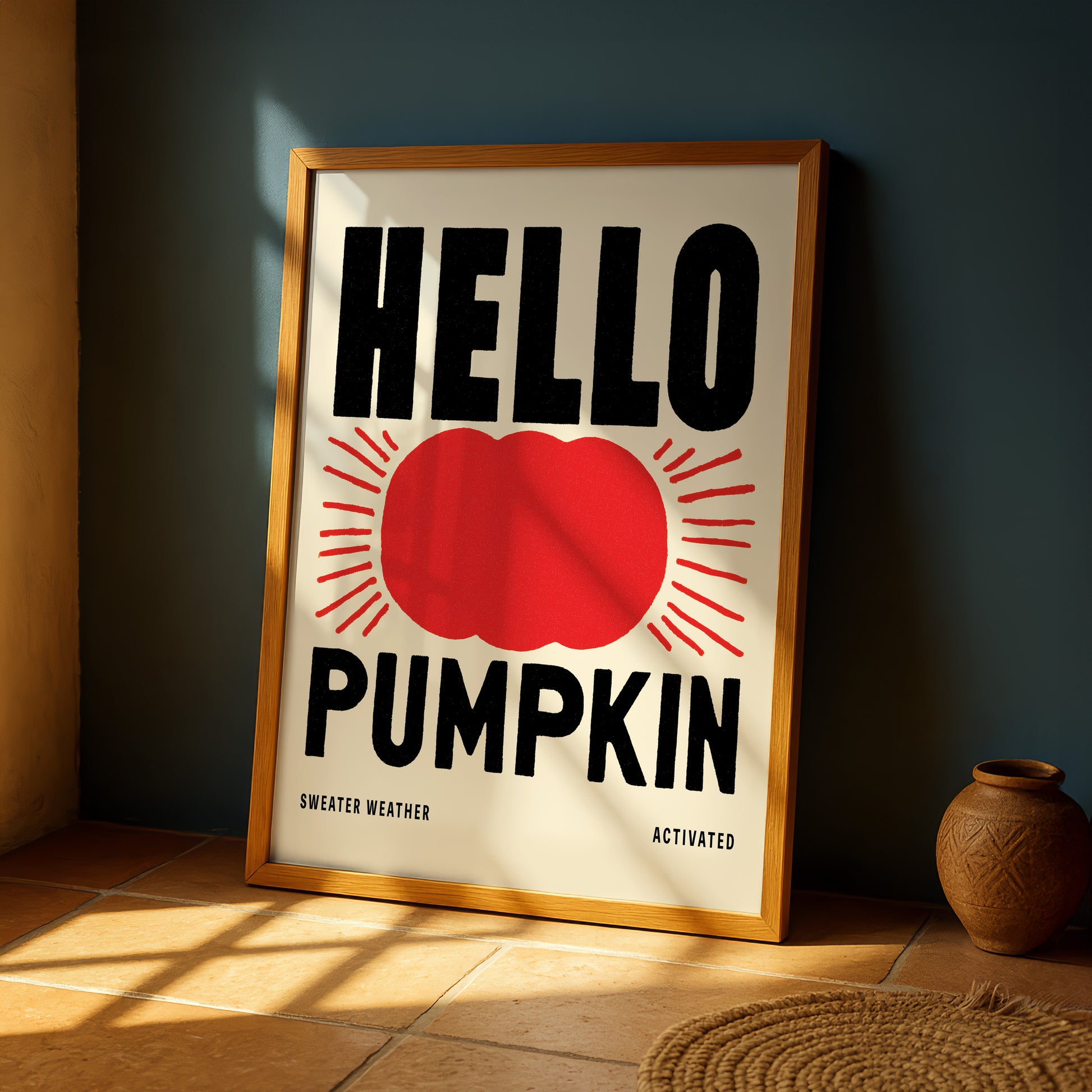 a framed poster with the text "HELLO PUMPKIN" and a red pumpkin graphic, placed on a tiled floor next to a vase.