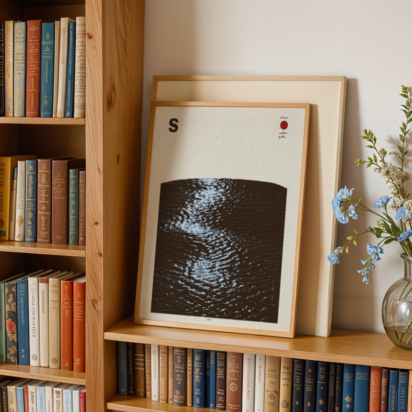 a wooden bookshelf filled with various books, a framed artwork depicting a black and white image of water, and a vase of blue flowers.