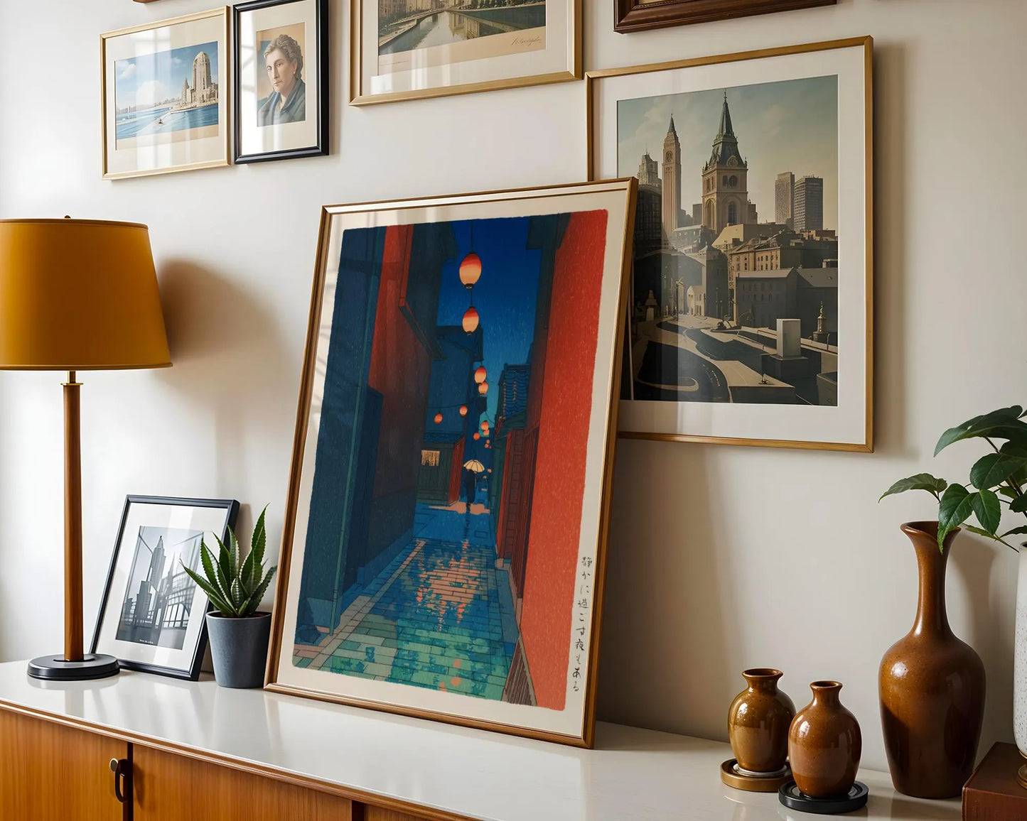 a wall adorned with framed artworks, including a large painting depicting a cityscape with a red building and orange lanterns. The artworks are arranged in a visually appealing manner, creating a harmonious and aesthetically pleasing display.