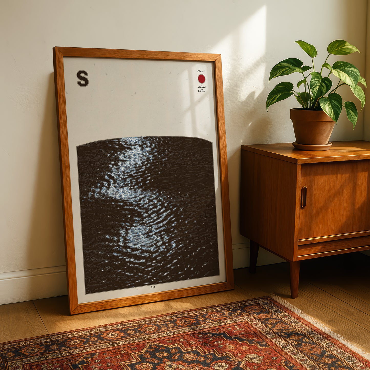 a framed artwork depicting a dark, wavy pattern, placed on a wooden floor next to a potted plant and a wooden cabinet.