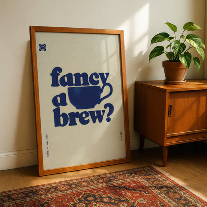 a framed poster with the text "fancy a brew?" and a blue cup icon, placed on a wooden cabinet next to a potted plant.