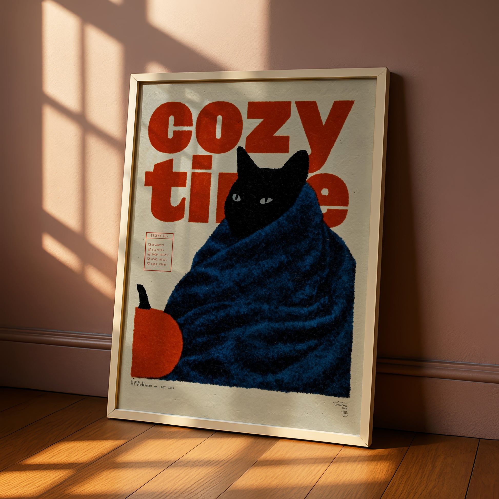 A framed poster with a black cat wrapped in a blue blanket, sitting on a wooden floor and looking out of a window.