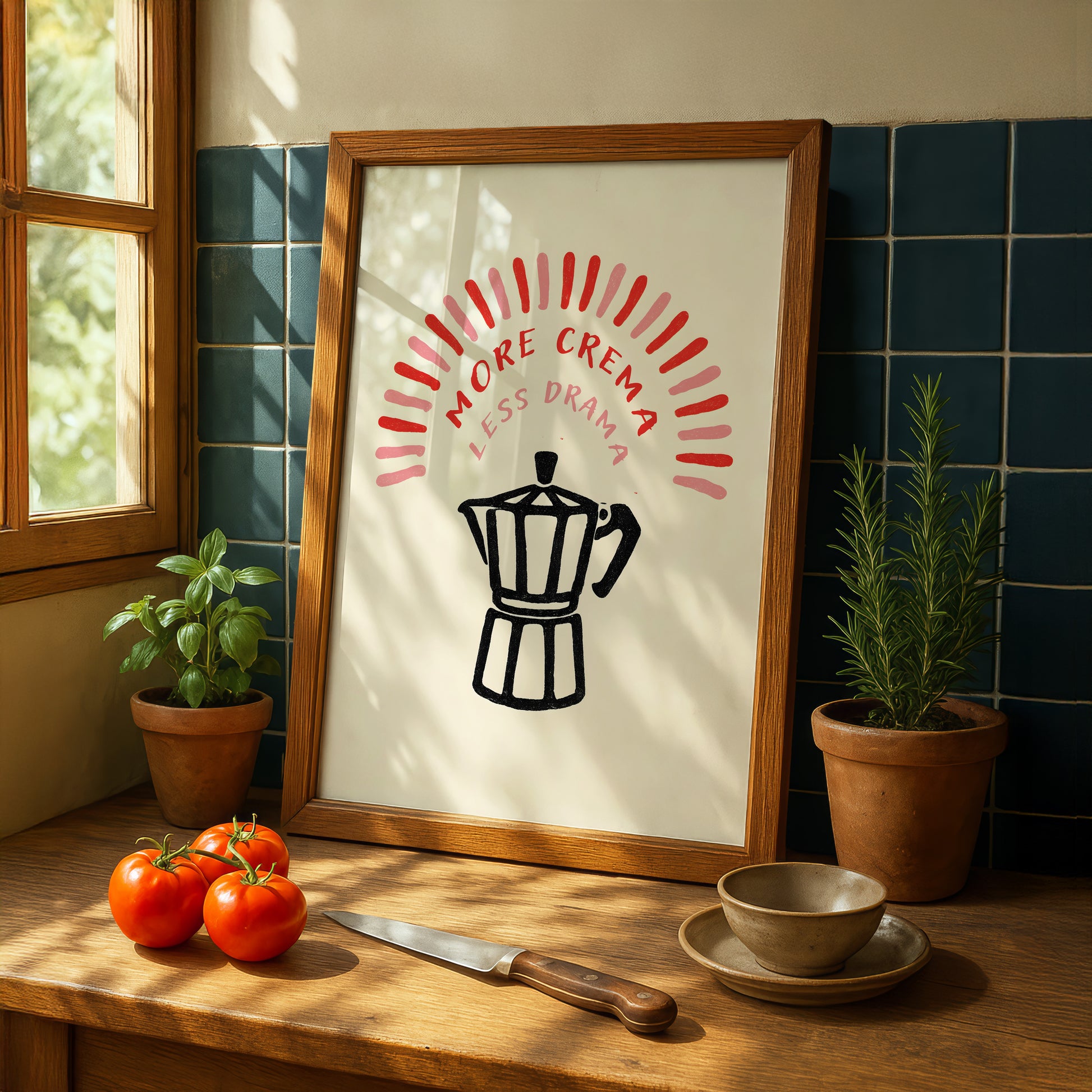a framed poster with a black and white illustration of a coffee maker, surrounded by a decorative border, placed on a wooden table. Next to the poster are a potted plant, a bowl, and a knife. The table also has a few tomatoes and a small plant.