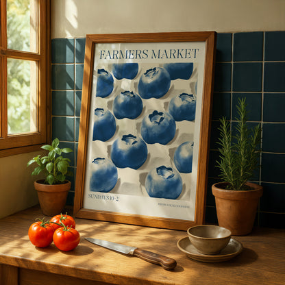 a framed poster of blueberries on a kitchen counter, with a knife, potted plants, and a bowl of fruit nearby.