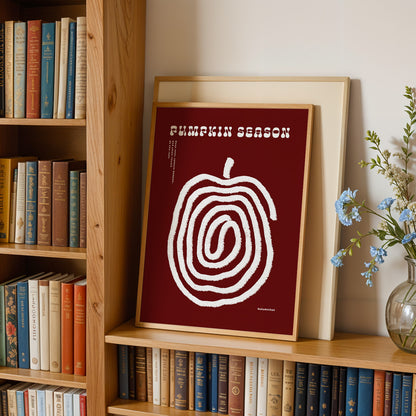 a bookshelf with a framed poster of a spiral design on the shelf, surrounded by various books. There is also a vase of flowers on the right side of the bookshelf.