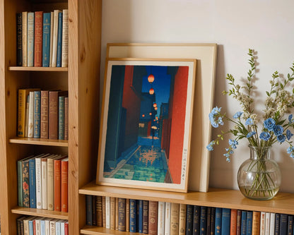 a bookshelf filled with books, a framed artwork depicting a city street at night, and a vase of blue flowers on the shelf.