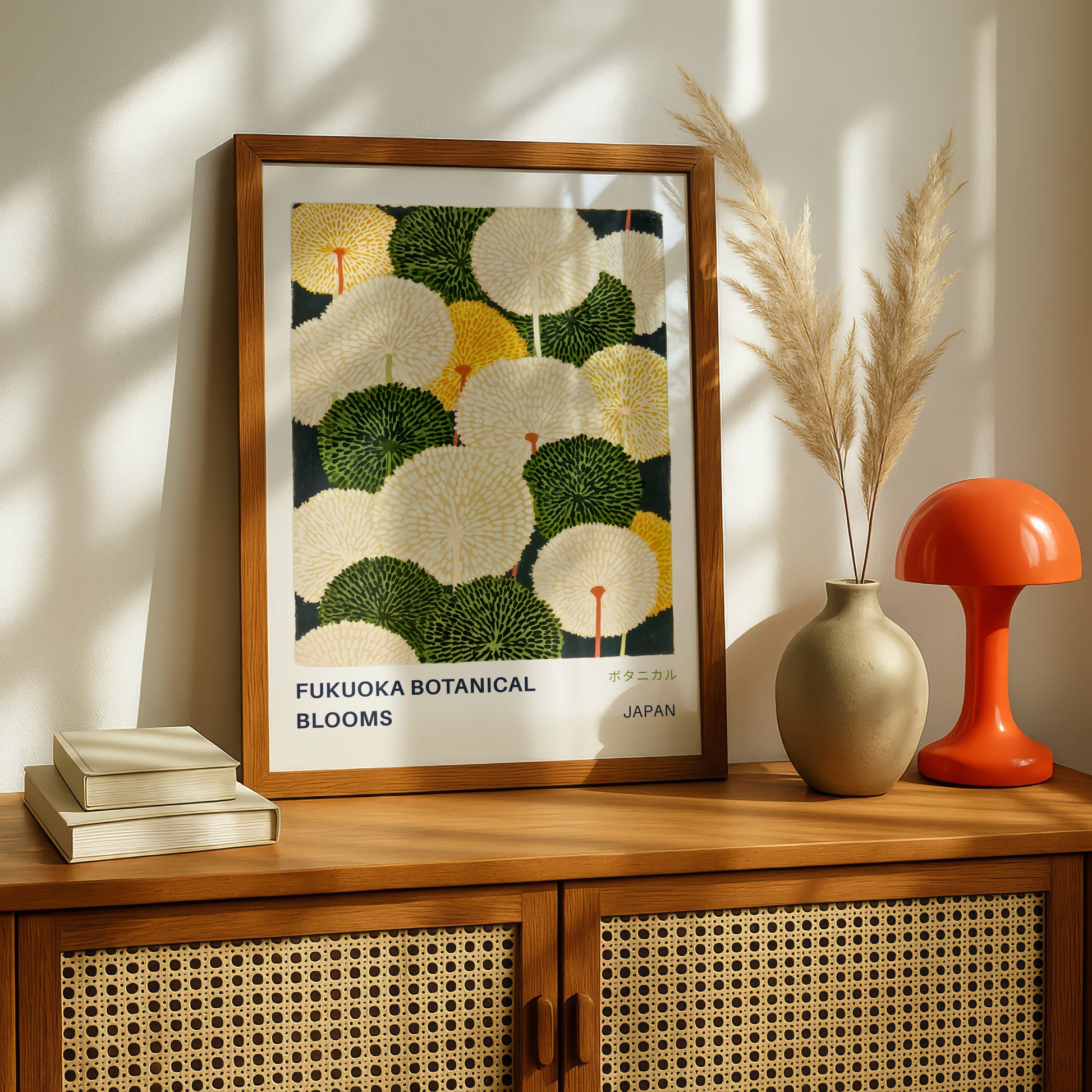a framed poster of a botanical illustration of flowers, placed on a wooden cabinet or shelf. Next to the poster, there is a vase with pampas grasses and a stack of books.