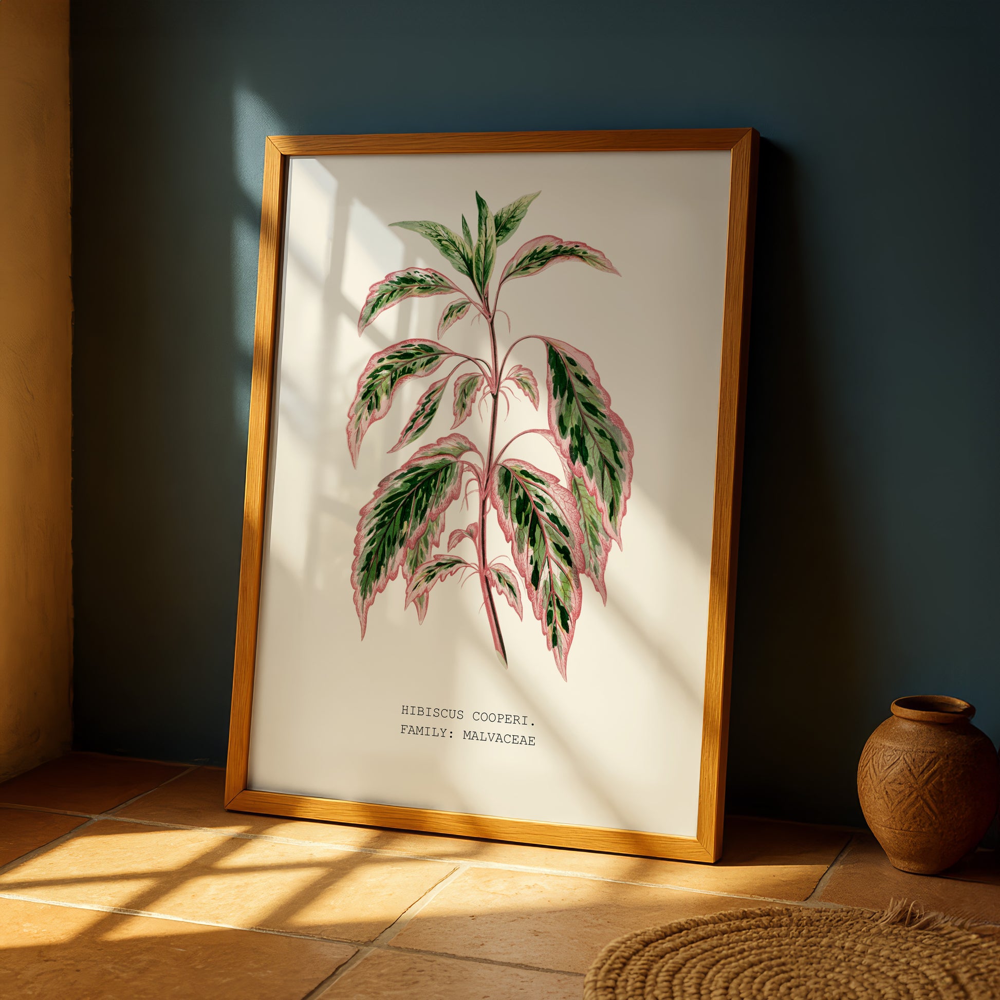 a framed botanical illustration of a plant with large leaves, placed on a wooden floor next to a vase.