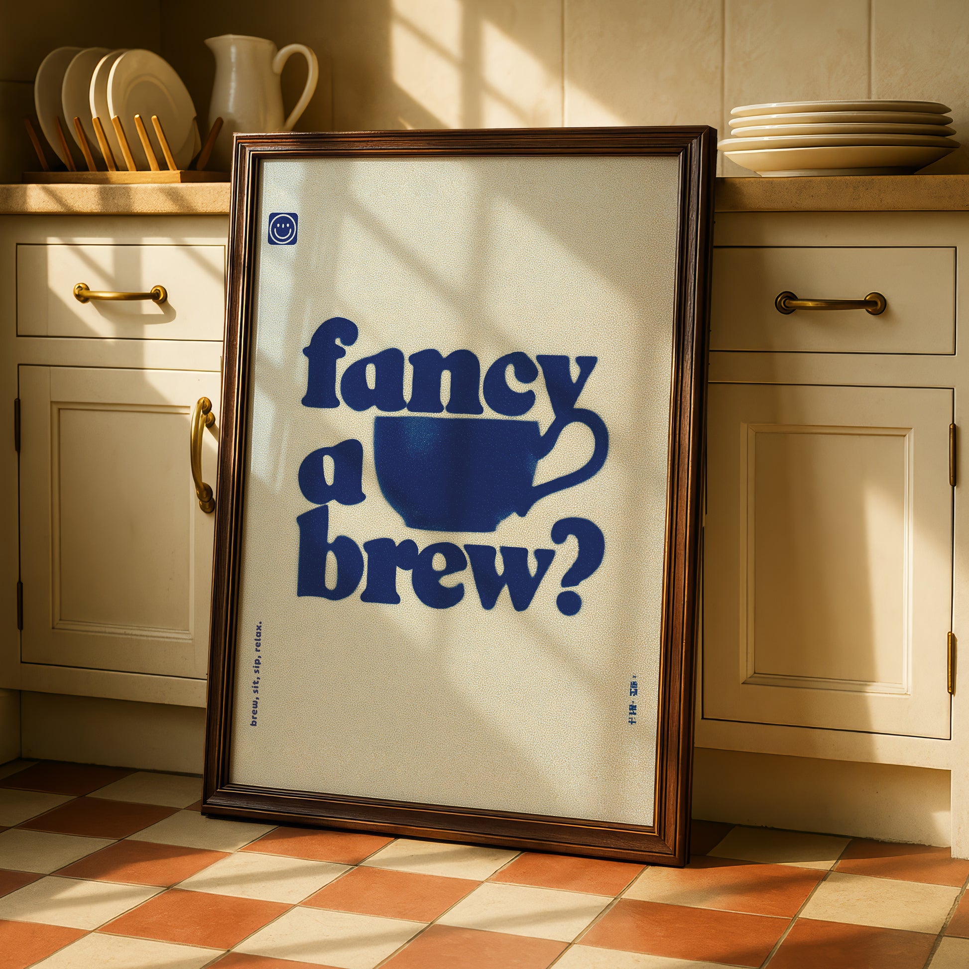 A framed poster with the text "fancy a brew?" displayed prominently in the center of the frame, placed on a checkered floor in a kitchen setting.