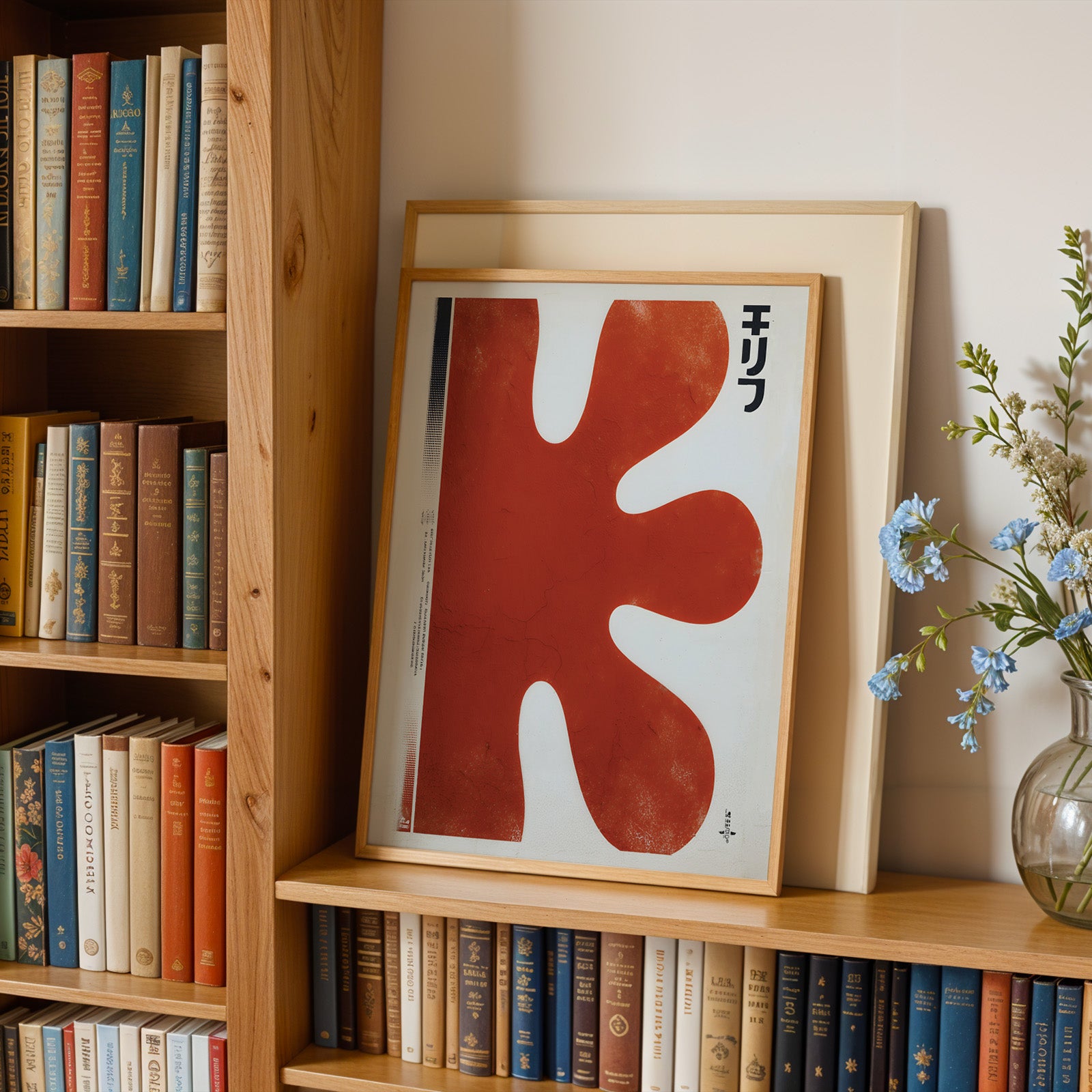 a wooden bookshelf filled with books, a framed artwork with a red abstract design, and a vase of blue flowers.