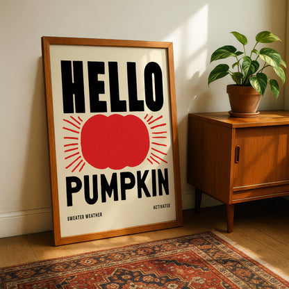 A framed poster with the text "HELLO PUMPKIN" and a red pumpkin graphic, placed on a wooden floor next to a potted plant.